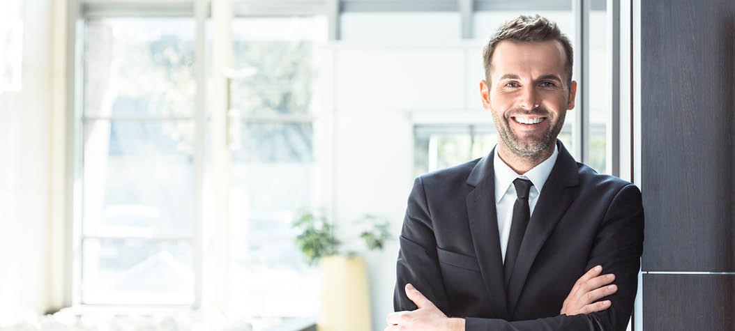 Portrait of happy businessman wearing suit standing with arms crossed in an office, smiling at camera 
