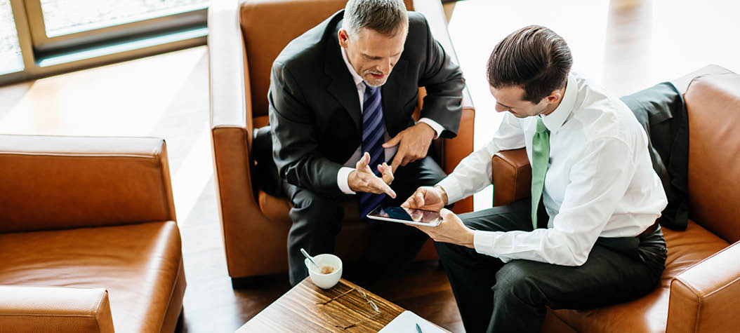 Two business partners sitting down at the office looking at a digital tablet and reviewing documents 